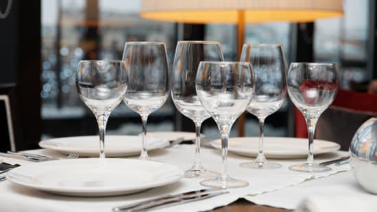Clean wine glasses of varying heights laid on a dining table with polished plates in a dining room.