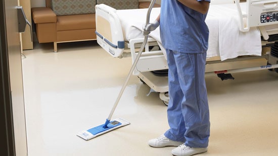 Hospital staff pushing an Ecolab microfiber mop across a hospital room floor under a bed.