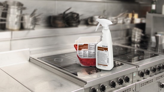 Greaselift spray bottle with a commercial sized bag of cleaning solution sitting on the  stovetop of a commercial kitchen.