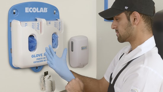 Food service employee stretching food prep gloves over his hand at an Ecolab glove station.