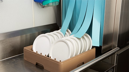A filled rack of plates coming out of a commercial dishwashing on a stainless-steel table.