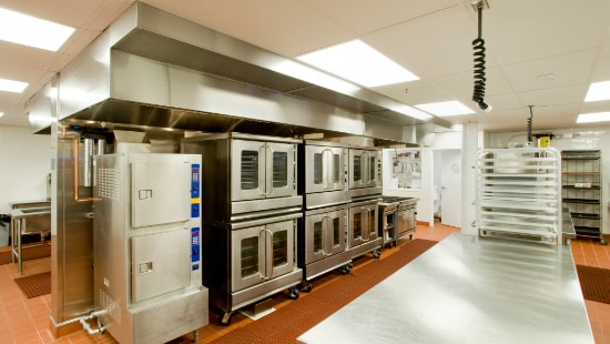 Clean and sanitized stainless steel commercial kitchen set-up with several ovens and oven racks.