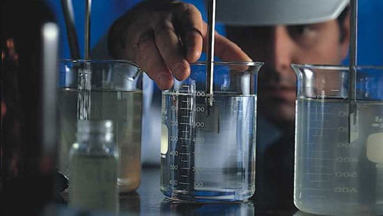 Engineer measuring the coagulation and flocculation of fluids in a beaker using an instrument.