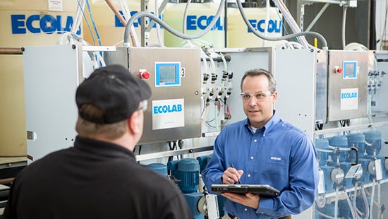 Commercial Laundry Consultant Speaking with Commercial Laundry Manager in front of Ecolab Laundry Equipment. 