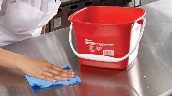Employee cleaning prep table in a commercial kitchen