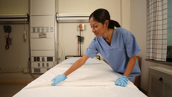 Hospital worker changing the white linens on surgical bed.