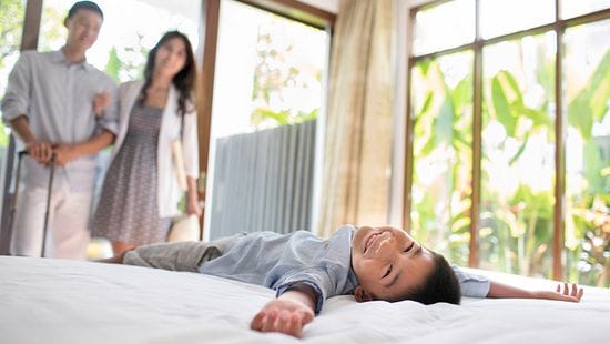 A couple looking at a child laying on clean linens in a hotel room