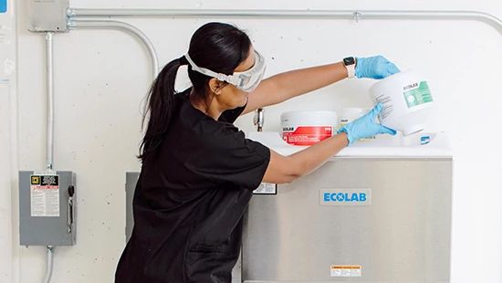 Hospitality associate pouring an Ecolab solid laundry product into a commercial laundry machine