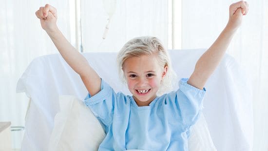 Child in hospital bed with arms up in celebratory way.