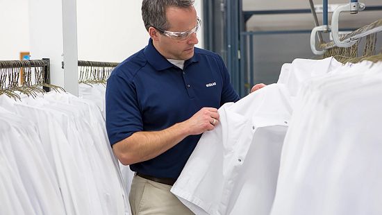 An Ecolab employee sorting through a rack of white lab coats. 